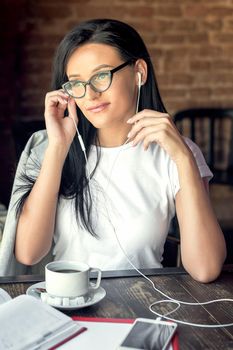 Beautiful smiling woman in glasses is listening music by her smartphone at cafe. Lifestyle concept