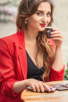 Portrait of young woman with cup drinking coffee at city street cafe.