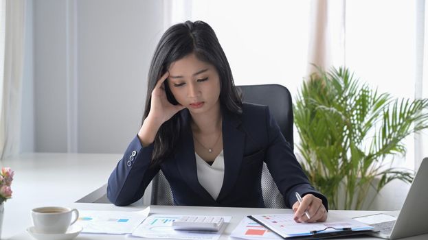Stressed female accountant checking financial document at office desk.