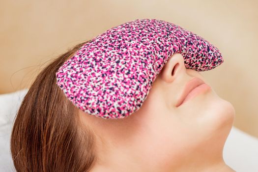 Restorative eye pillow covers eyes of young woman while relaxing on bed.