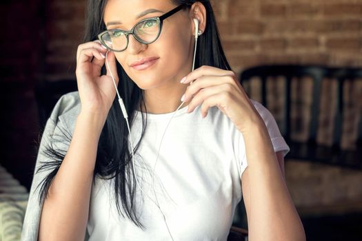 Beautiful woman listening music through headphones wearing eyeglasses smiling in cafe.