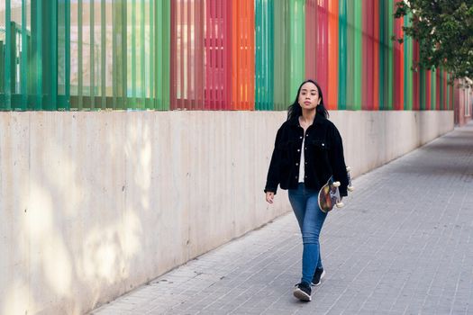 asian teenage girl walking down the street with her skateboard in her hand