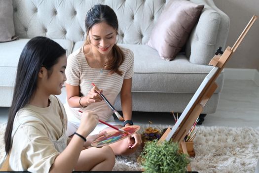 Asian mother with little daughter painting and spending leisure time together at home.