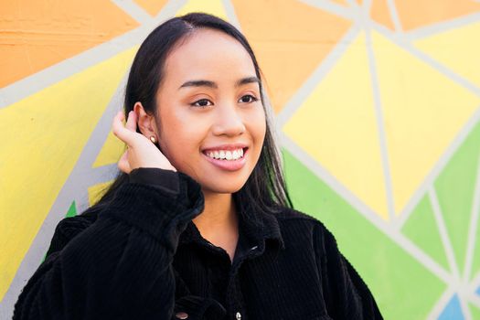 cheerful young asian woman smiling leaning against a colorful wall