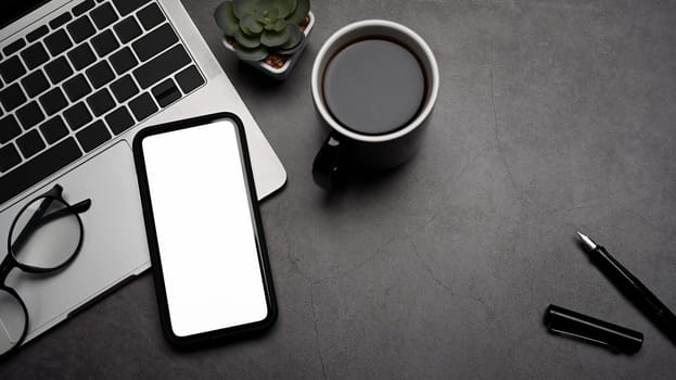 Modern workplace with mobile phone, laptop computer and coffee cup on black background.