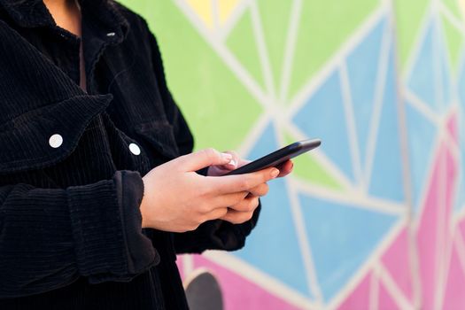 close up of the hands of an unrecognizable young woman typing on her cell phone against a colorful wall