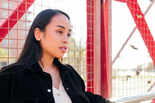 portrait of a young asian woman outdoors leaning against a red fence