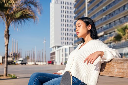 young asian woman relaxing sitting on a street bench sunbathing