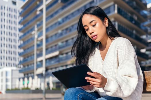asian young woman sitting on the street using her tablet