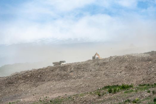 Backhoe working on garbage dump in landfill. People Working at Landfill site.