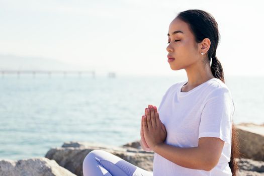 portrait of a young asian woman meditating outdoors in calm with hands together and eyes closed, concept of spirituality and relax