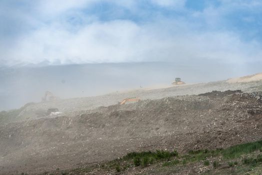 Backhoe working on garbage dump in landfill. People Working at Landfill site.