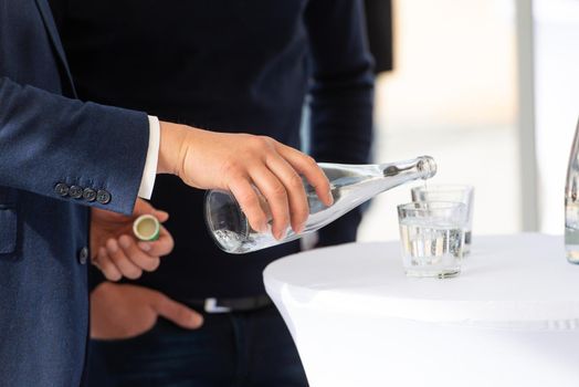 man in a suit pouring water from bottle to glass.