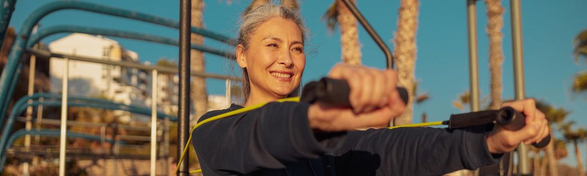 Happy female in hoodie training in outdoor street gym, with arms extended forward doing arms stretching