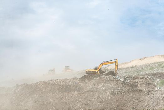 Backhoe working on garbage dump in landfill. People Working at Landfill site.