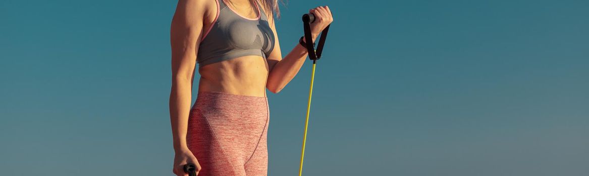 Portrait of mature happy lady doing stretching of arms muscles using fitness rubber bands next to the embankment