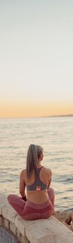 Vertical photo of woman in sports clothing sitting by the sea enjoying sunset in the evening