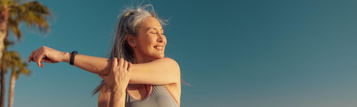 Active female in sportswear doing arm workout on the sports ground on a sunny day by the waterfront