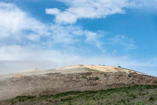 Backhoe working on garbage dump in landfill. People Working at Landfill site.