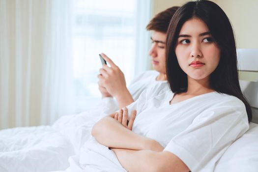unhappy young asian couple have problems in relationships, boyfriend playing games on mobile phone on bed.