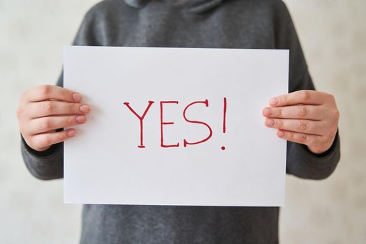 Girl holds a sheet of paper with the inscription YES. The inscription YES in the girl's hands on a white sheet