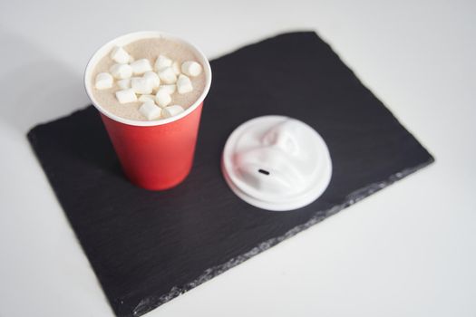 Red paper cup of coffee with marshmallows on a black tray. High-quality photo