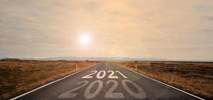 The word 2021 written on highway road in the middle of empty asphalt road at golden sunset and beautiful blue sky. Concept 2021
