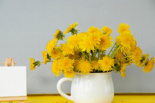 bouquet of yellow dandelions in a white mug on a gray background with space for your text. flat lay with floral and summer background. copy space. soft focus