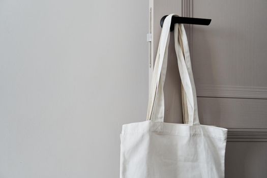 Eco friendly concept with white canvas tote bag hanging on door knob with two toned colored, Eco blank shopping sack with free copy space, Reduce plastic bags to reduce global warming. Canvas tote bag