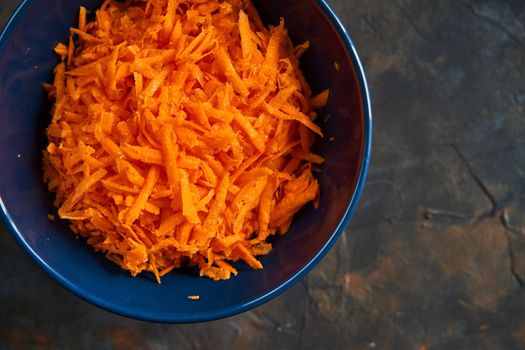 Grated carrots in a blue plate on a dark background. Carrot salad. Healthy breakfast.