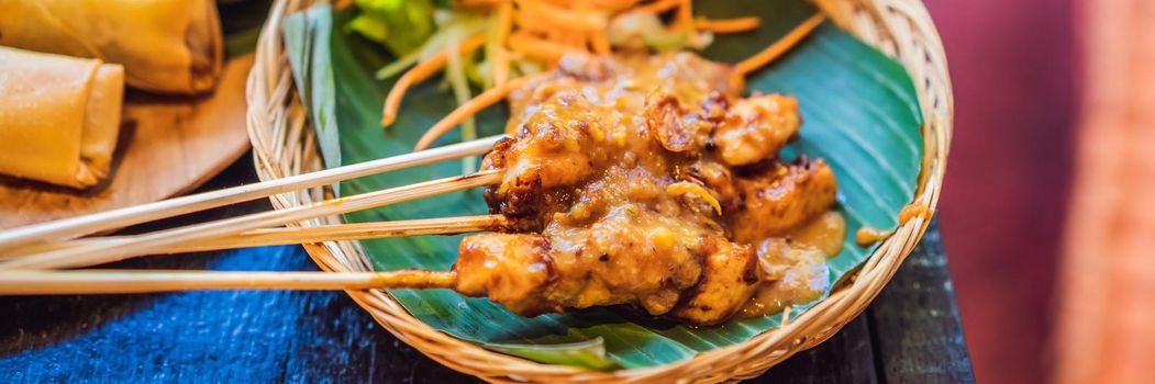 Satay or sate, skewered and grilled meat, served with peanut sauce, cucumber and ketupat. Traditional Malaysian and Indonesian food. Delicious hot and spicy Malaysian dish, Asian cuisine. BANNER, LONG FORMAT