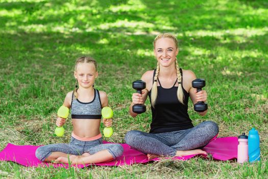 Young mother with her little daughter are training with apple dumbbells in the park.