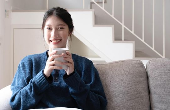 Portrait of smiling happy cheerful beautiful pretty asian woman relaxing drinking and looking at camara.Girl felling enjoy having breakfast in holiday morning vacation on sofa at home.