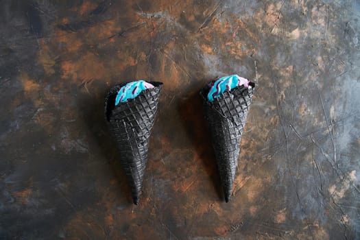 Two black waffle cones of ice cream on a dark background, top view. Trendy ice cream