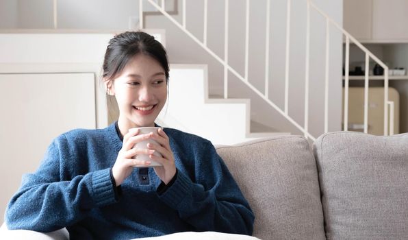 Portrait of smiling happy cheerful beautiful pretty asian woman relaxing drink. Girl felling enjoy having breakfast in holiday morning vacation on sofa at home.