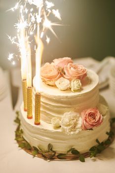 White wedding cake with burning candles at wedding celebration close-up. High quality photo