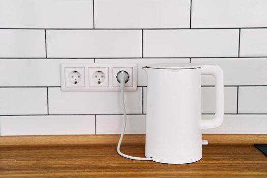 White stylish electric kettle stands on a wooden kitchen countertop. High quality photo