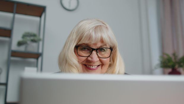 Senior mature older business woman wears glasses remote working, social distance elearning, training, online webinar at home office, using laptop computer. Close-up face elderly grandmother freelancer