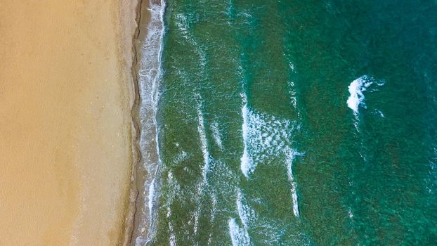 Aerial top view of sea waves hitting rocks on the beach with turquoise sea water. Amazing rock cliff seascape in the Portuguese coastline. Drone shot