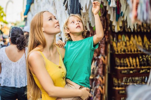 Mom and son travelers choose souvenirs in the market at Ubud in Bali, Indonesia.