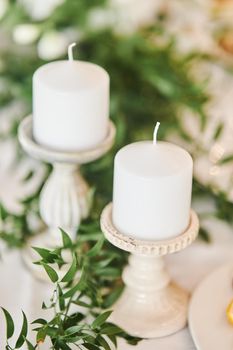 White candles in candlesticks at a wedding celebration. High-quality photo