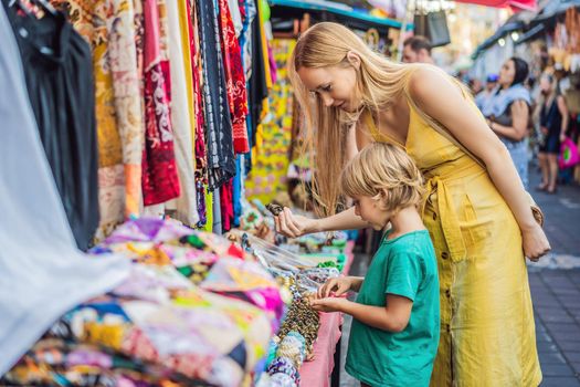 Mom and son travelers choose souvenirs in the market at Ubud in Bali, Indonesia.