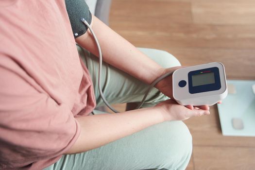 Selective focus girl is taking care for health with hearth beat monitor and blood pressure and heart rate monitor with digital pressure gauge. Health care and Medical concept. The topic of high blood pressure is hypertension disease. Close-up macro young caucasian woman hands using automatic tonometer to check pressure at home in bedroom on bed.