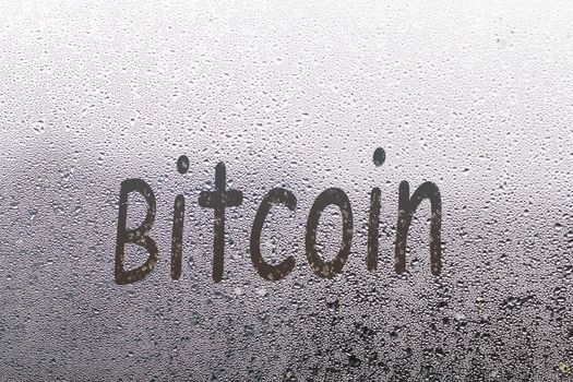 bitcoin handwritten on wet glass of night window.