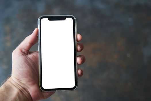 Kaliningrad, Russia - 08.08.2020: A young man holds in his hand a modern smartphone with a white screen on a dark background. Design Mockup.