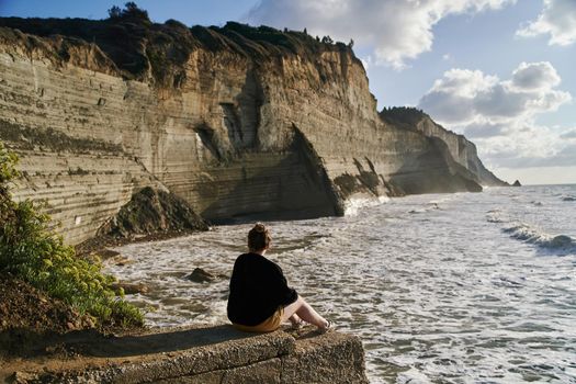 Young woman sits on a stone and admires the sea and rocks. High quality photo