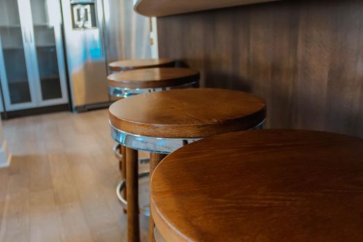Row of retro wooden stools in front of wooden counter inside a modern style kitchen. Side view