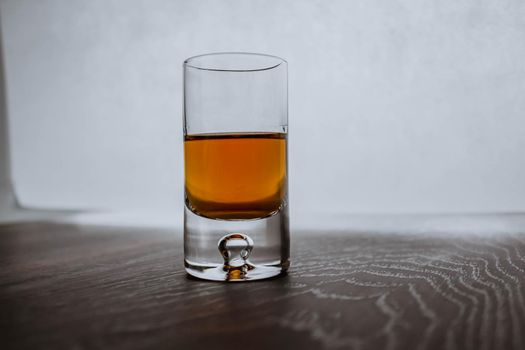 One shot of glass with whiskey on a wooden background