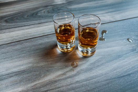 Two shot glasses with whiskey on a wooden background