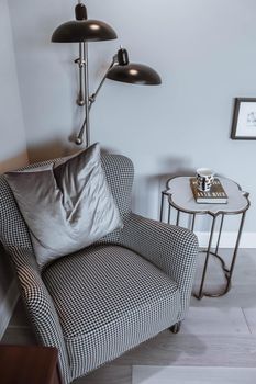 A reading chair armchair with a lamp, blanket and a open book. Empty white wall in simple living room interior. Copy space